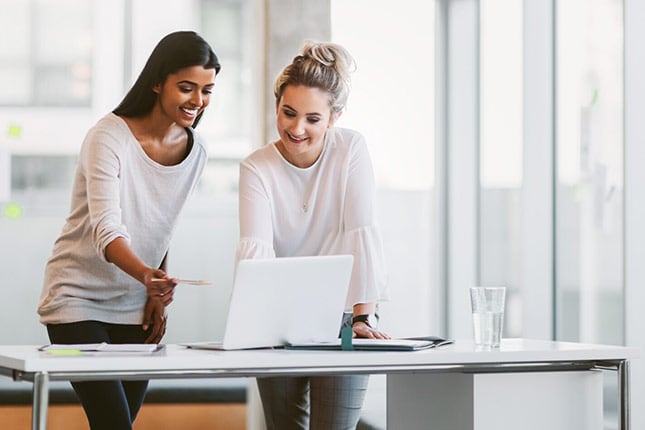 Business woman and colleague standing in front of desk and working on laptop in modern business office