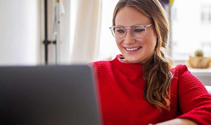 Woman wearing glasses and a red sweater smiles at her computer screen