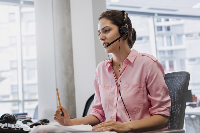 Woman with hands-free device talking on telephone at office desk.