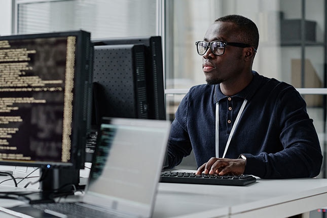Security analyst reviewing system logs on multiple monitors to support human oversight and immutable audit trails.