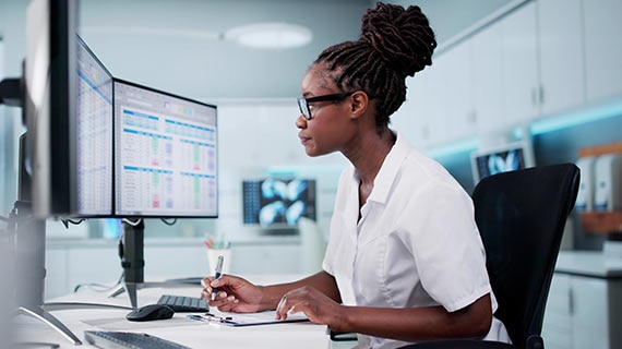 Compliance professional reviewing audit and risk dashboards on dual monitors to reduce manual workload and improve regulatory alignment..
