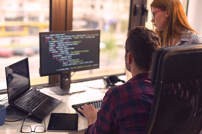 Data analysts reviewing monitoring code on a desktop screen to support predictive analytics, risk tracking, and trend analysis.