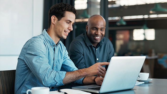 Two professionals collaborate at a workstation with code on multiple monitors, illustrating data governance framework implementation and data quality management.