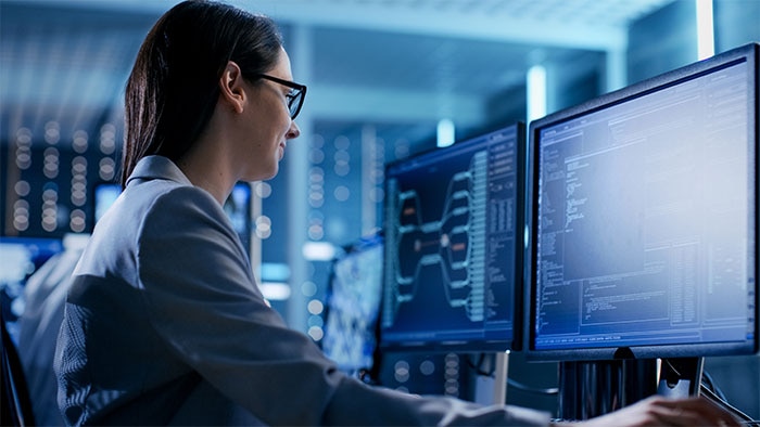 Professional working at multiple computer monitors displaying data analytics dashboards and enterprise systems in a modern data center environment, illustrating data governance and business data management.