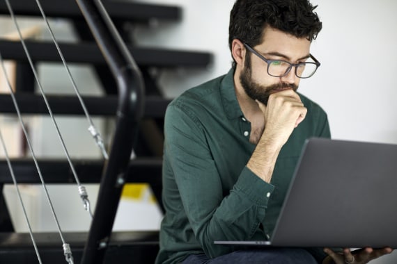 Male IT architect using laptop computer while sitting on steps in office.