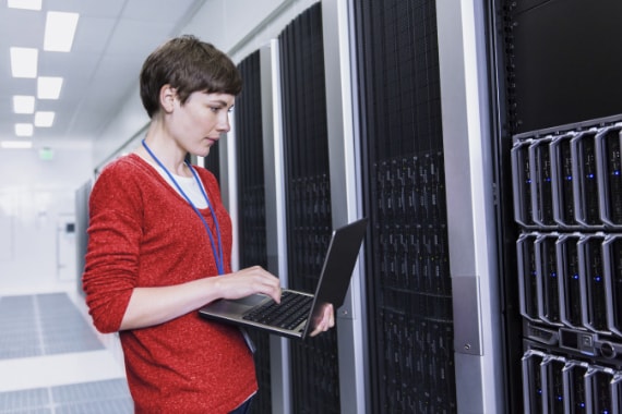Female IT professional working using a laptop computer in a modern server room.