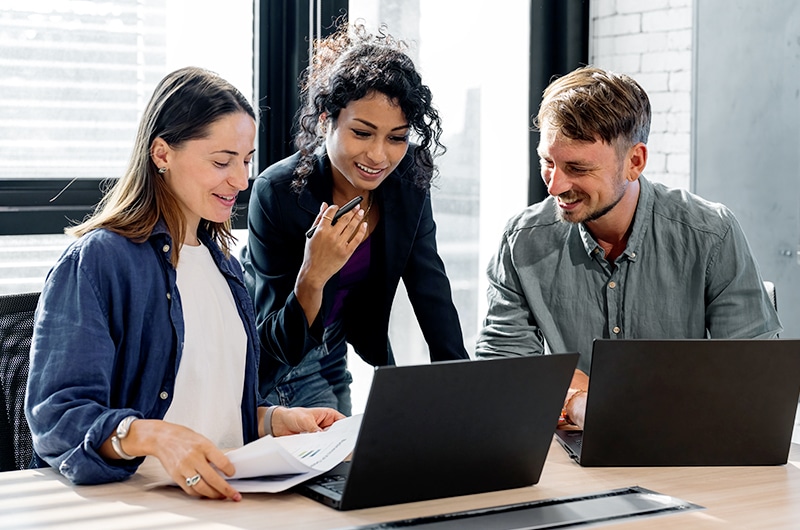 Coworkers with laptops in bright office discussing AI solutions.