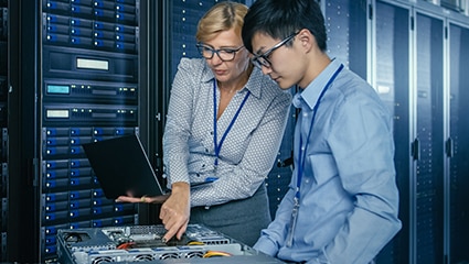 Two persons standing in a data center looking over an open server.