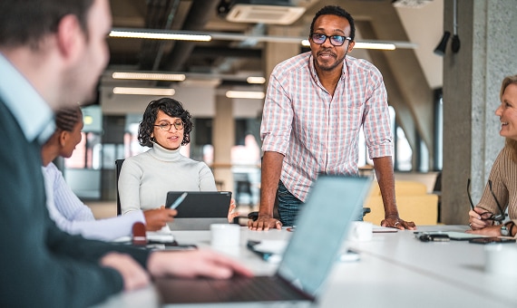 Team collaborating around a conference table while reviewing information on laptops and tablets.