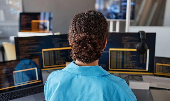 Developer monitoring code across multiple screens in a technology workspace.