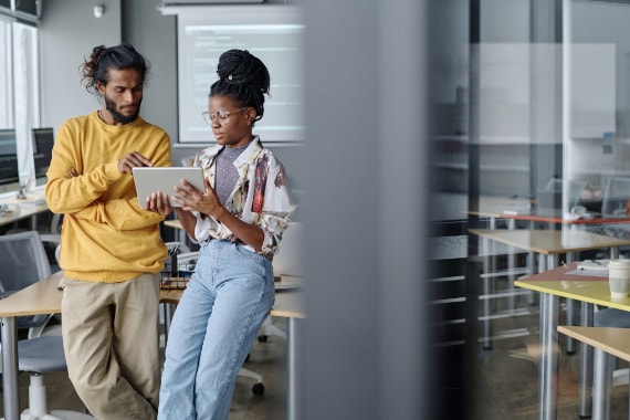 Two people in office discussing information on a tablet device.