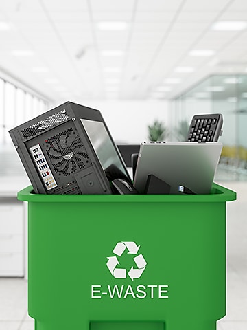 A pile of computers and monitors sit in a bright green recycling bin