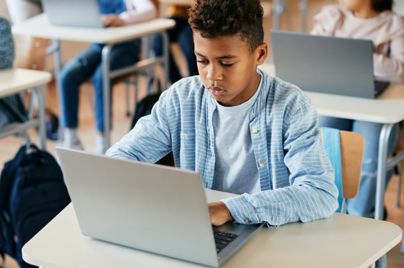 Young student is using his laptop in the classroom.