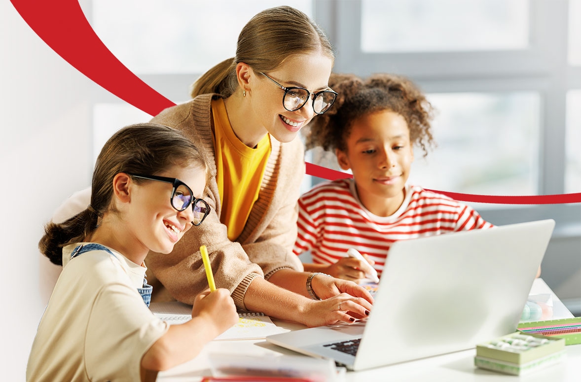 Teacher and two school children smiling and watching educational video on laptop during the lesson in a classroom