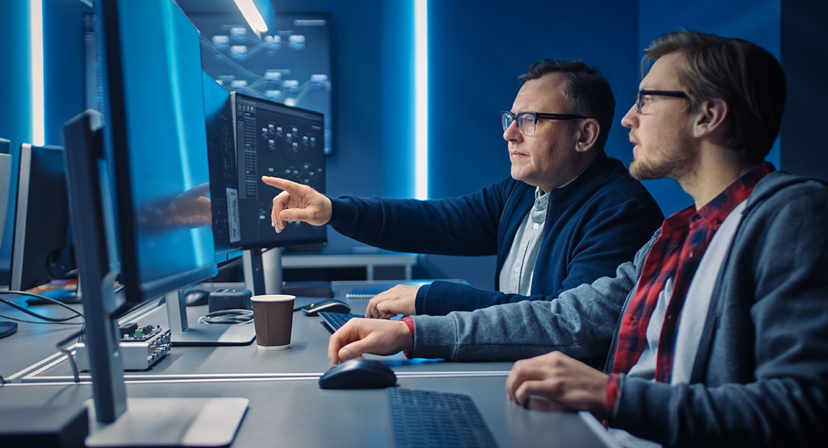 Two men looking at a computer monitor one of them is pointing at