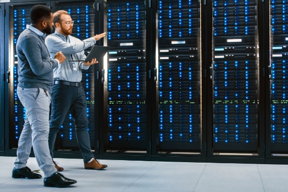 An IT professional, carrying a laptop, guides a client through a data center.