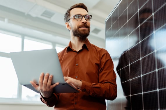 Man standing beside a solar panel, using a laptop to present solutions.