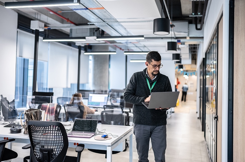 IT professional standing in office, using laptop to manage systems or troubleshoot issues.