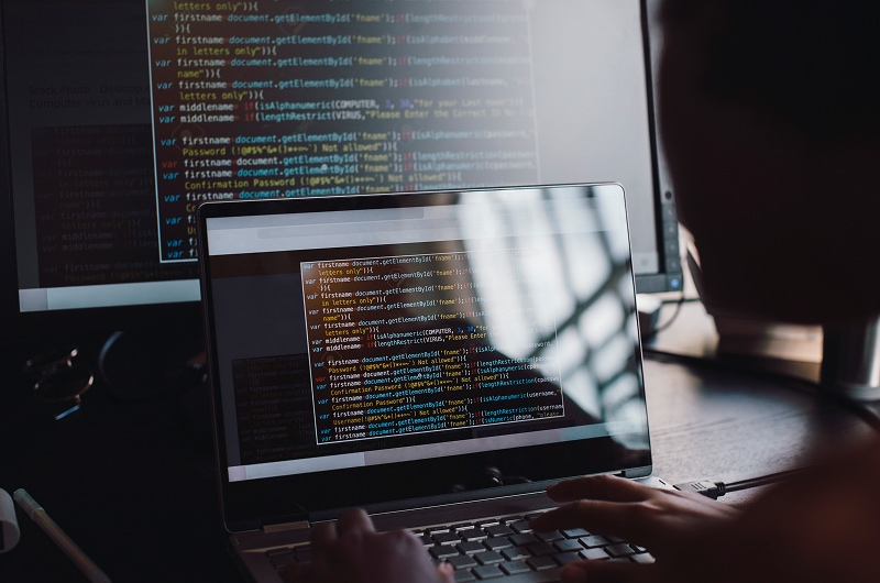 Close-up of computer screens with code and person working.