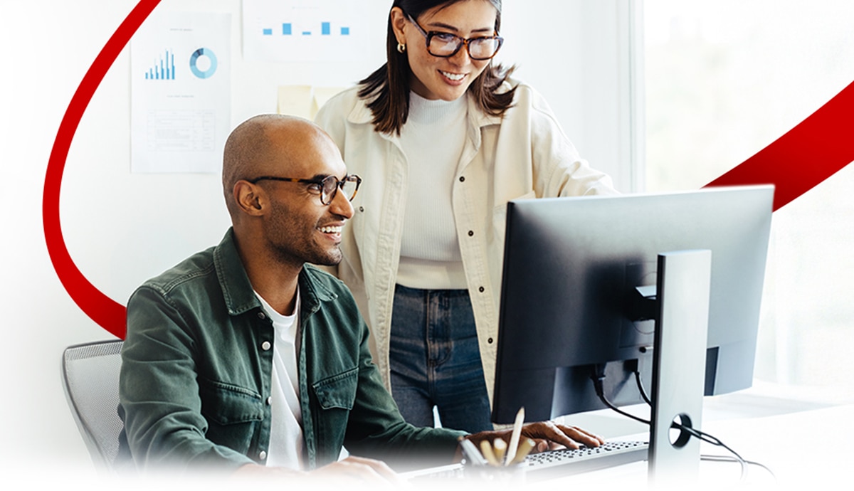 Coworkers interacting while working on a computer with a partial red orbit in the background.