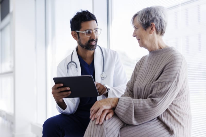 Physician using a tablet while talking to a patient.