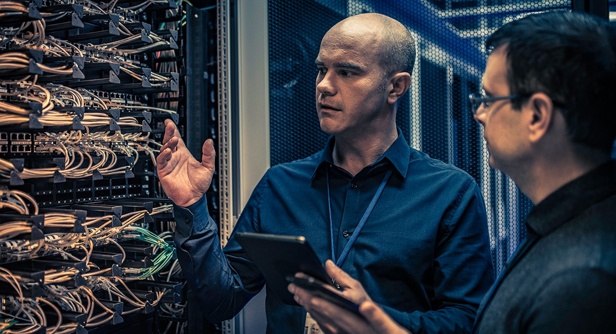 Two men looking at router wires in a data center