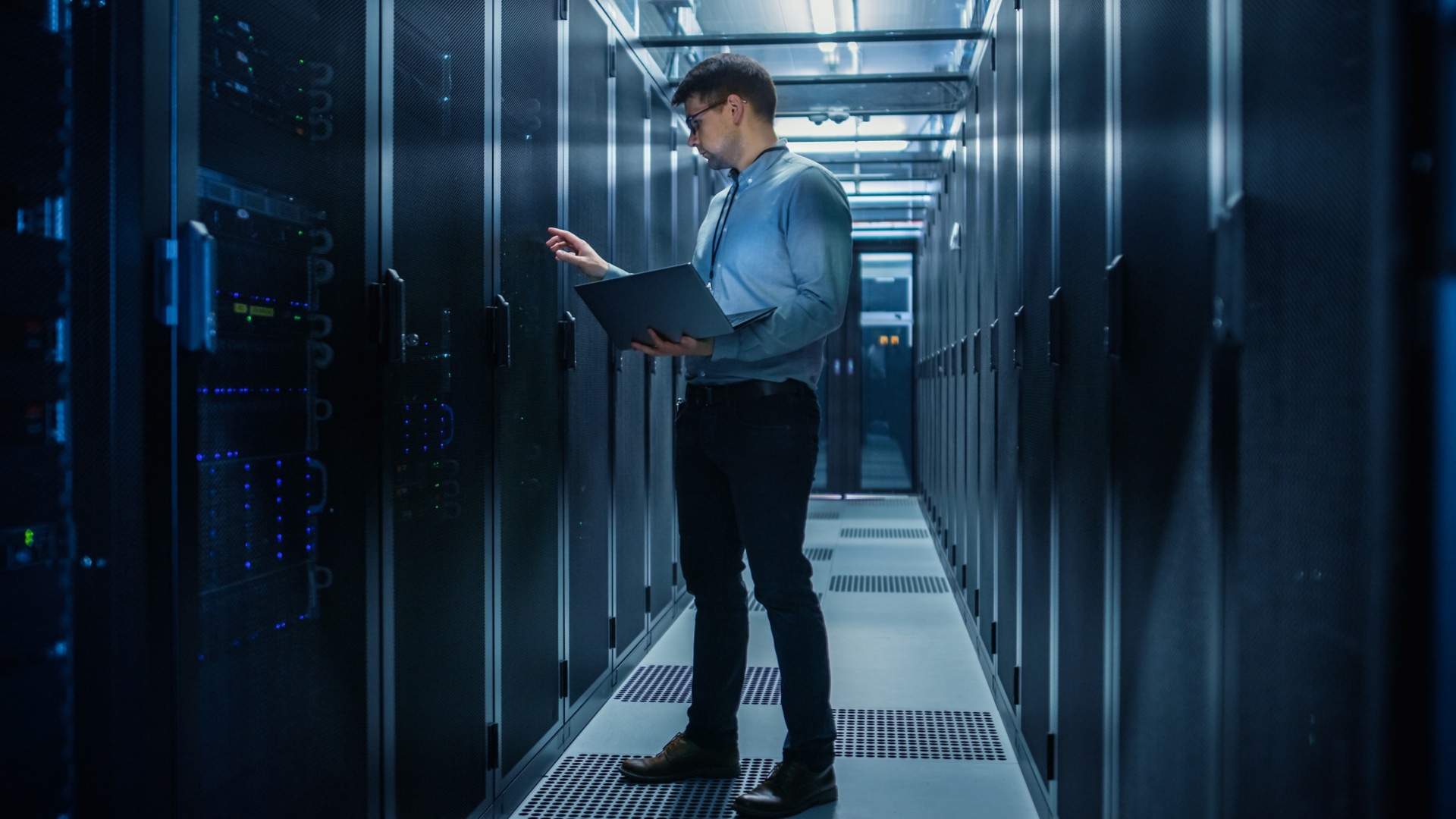 In Data Center IT Engineer Stands Before Working Server Rack Doing Routine Maintenance Check and Diagnostics Using Laptop. Concept of Cloud Computing, Artificial Intelligence, Supercomputer