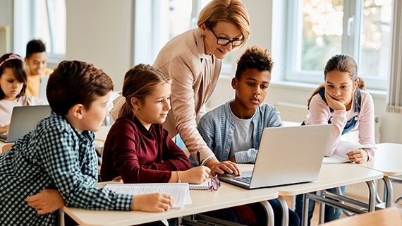 Teacher with students in bright office looking at laptops.
