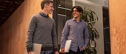 two men walking down modern office all with laptops