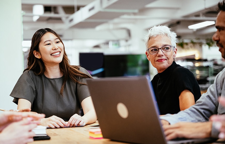 A teamwork between senior and mid-adult colleagues and business people, collaborating on a project at a modern office table surrounded by natural light