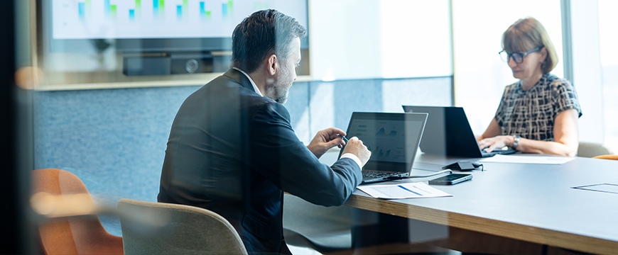 Older man working on a laptop along side middle aged female working on laptop.