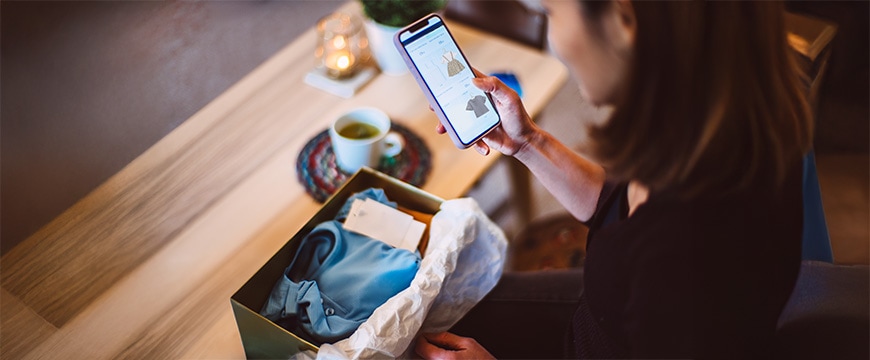 TitleYoung woman doing online shopping for clothes on smartphone at home