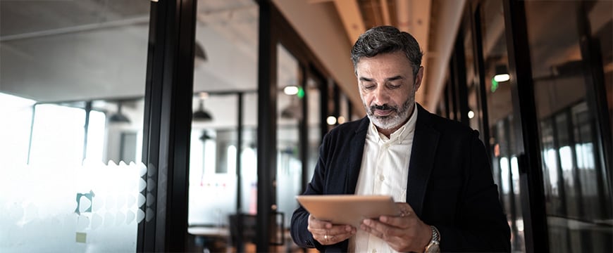 Mature businessman walking and using digital tablet at corridor office