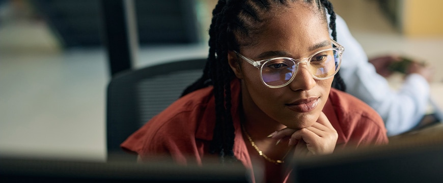 Young woman programmer focused on her work, coding on dual monitors in a modern office environment