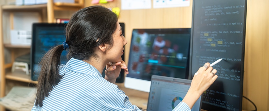 Woman in office, writing on interactive monitor screen displaying code.