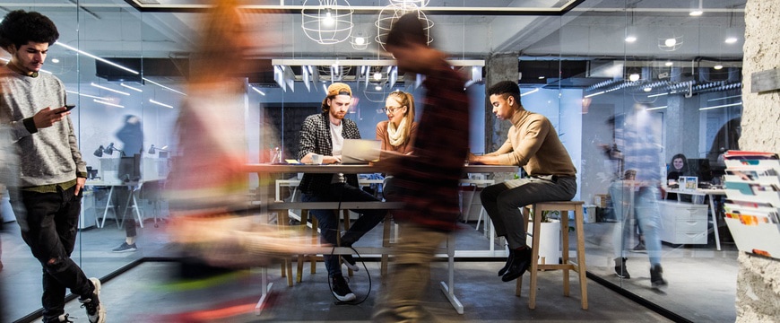 Team collaborating on laptop inside modern office with motion blur foreground.
