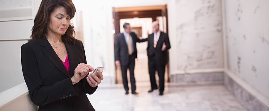 Goverment representative woman on phone in foreground; two government representative men in background within a federal or municipal building. 