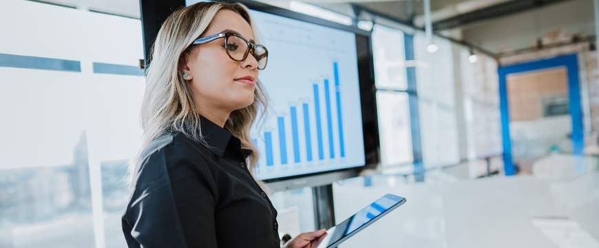 Professional presenting data on screen while holding tablet in modern office.