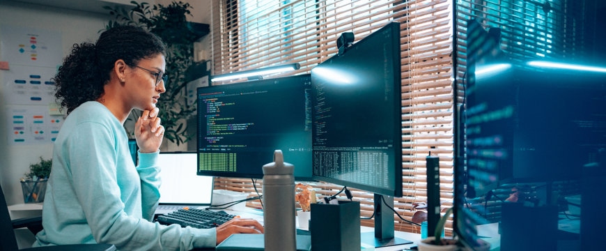 Person working at dual monitors with code displayed in a home office.