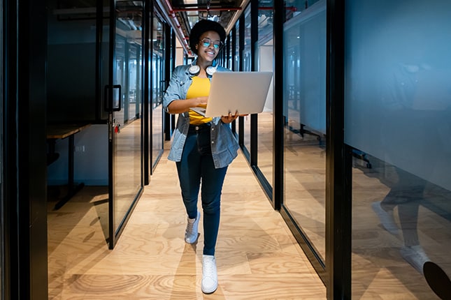 College student working from her laptop while walking in the classroom hallway.