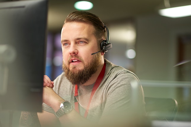 Man wearing headset speaking with a customer while working on a computer.