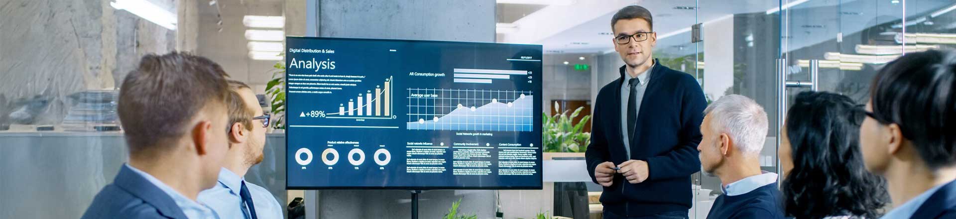 Young Stock Trader Shows to the Executive Managers Cryptocurrency and Trade Market Correlation Pointing at the Wall TV. image