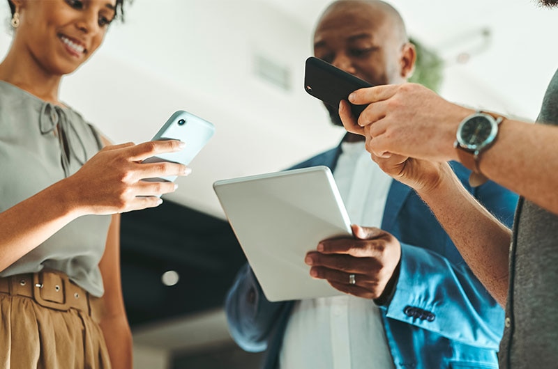 Professionals using multiple devices including smartphones and a tablet in a modern workspace, representing a unified AI experience across devices powered by Intel and CDW.