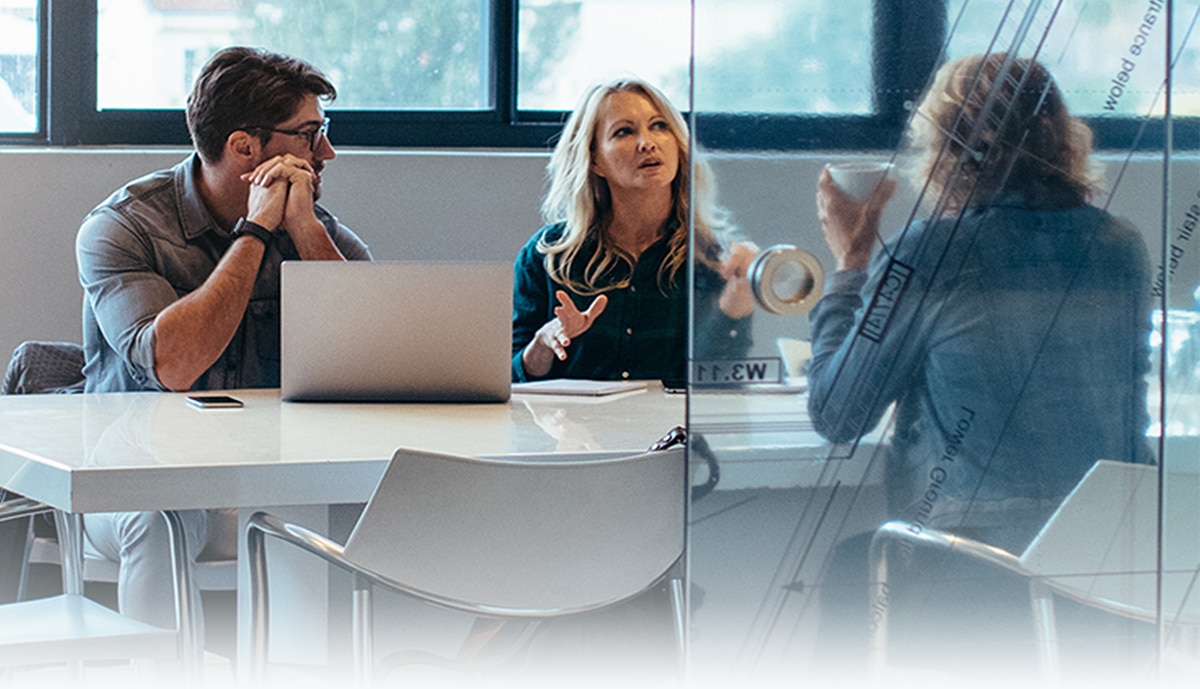 hero image of 3 employees talking during a meeting inside a glass office space.