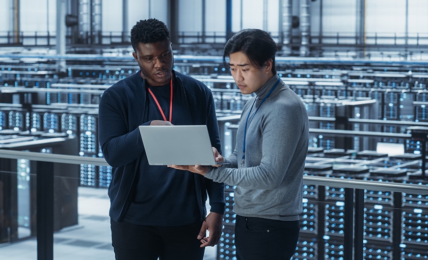 Two programmers collaborating on a laptop in a data center.