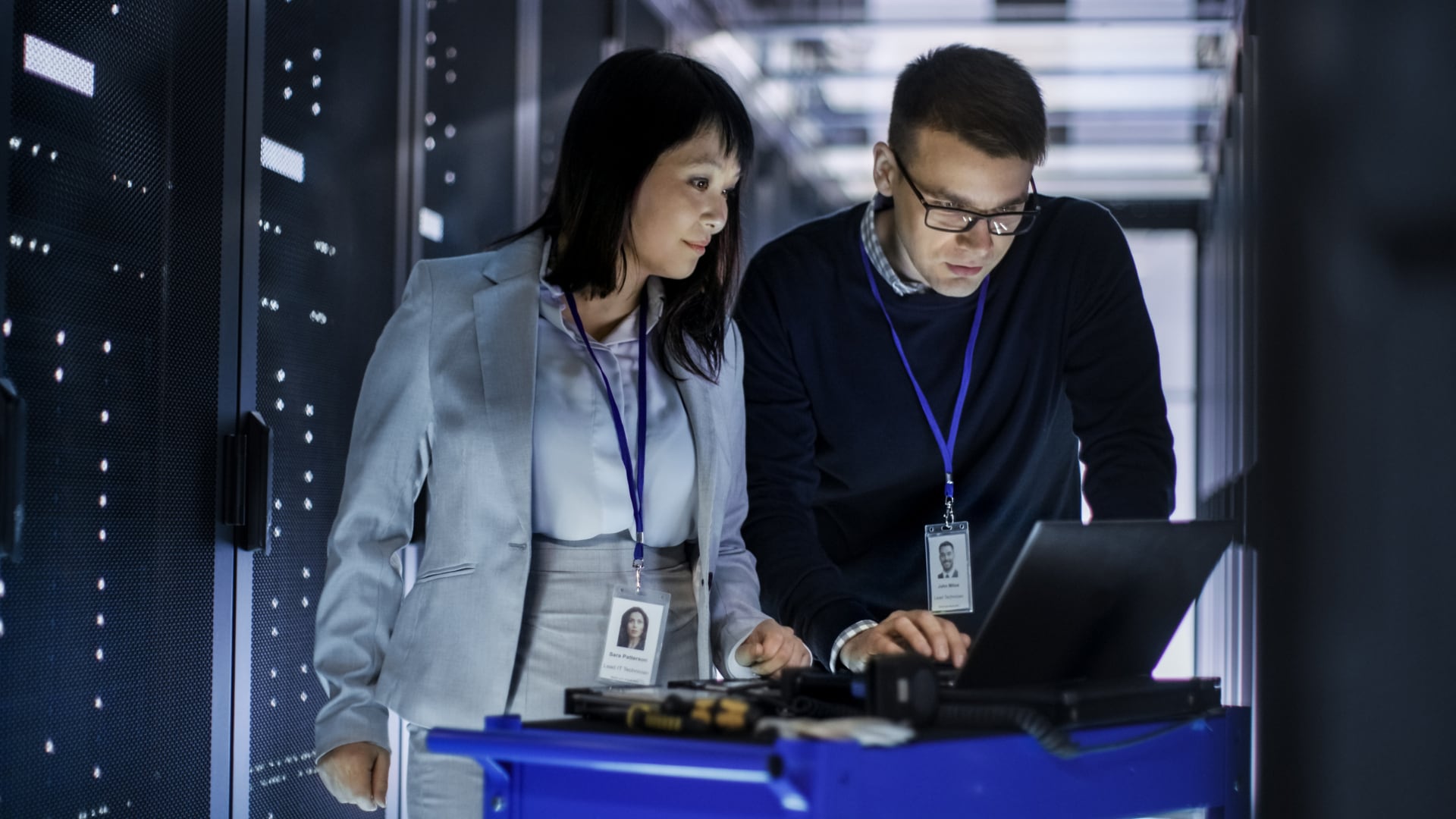 Caucasian Male and Asian Female IT Technicians Working with Computer Crash Cart in Big Data Center full of Rack Servers.