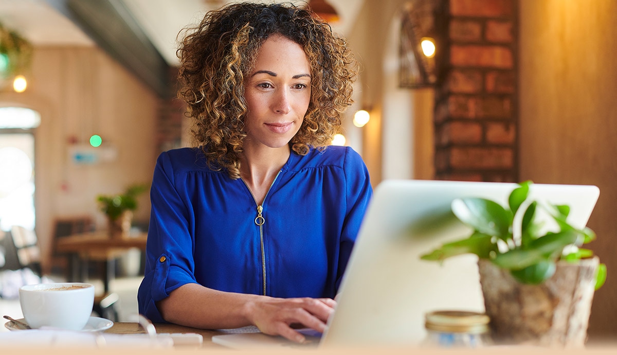 A professional woman working on a laptop in a modern café setting, representing the ease of managing Apple devices with Jamf.