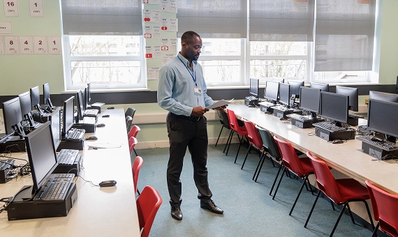 IT professional standing in a computer lab reviewing devices and classroom setup.