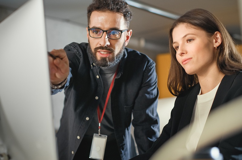 Two professionals reviewing content on a desktop monitor during a collaborative discussion.