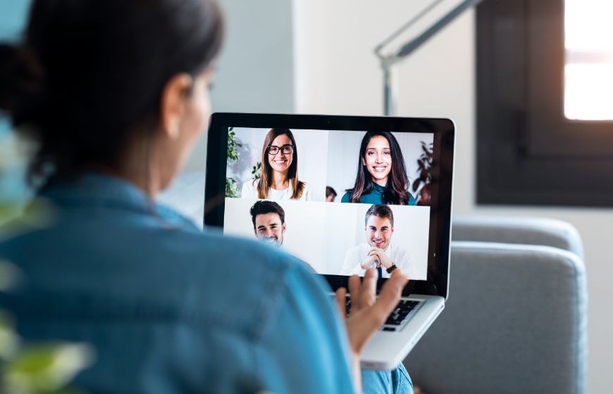 Back view of business woman speaking on video call with diverse colleagues on online briefing with laptop on sofa at home.